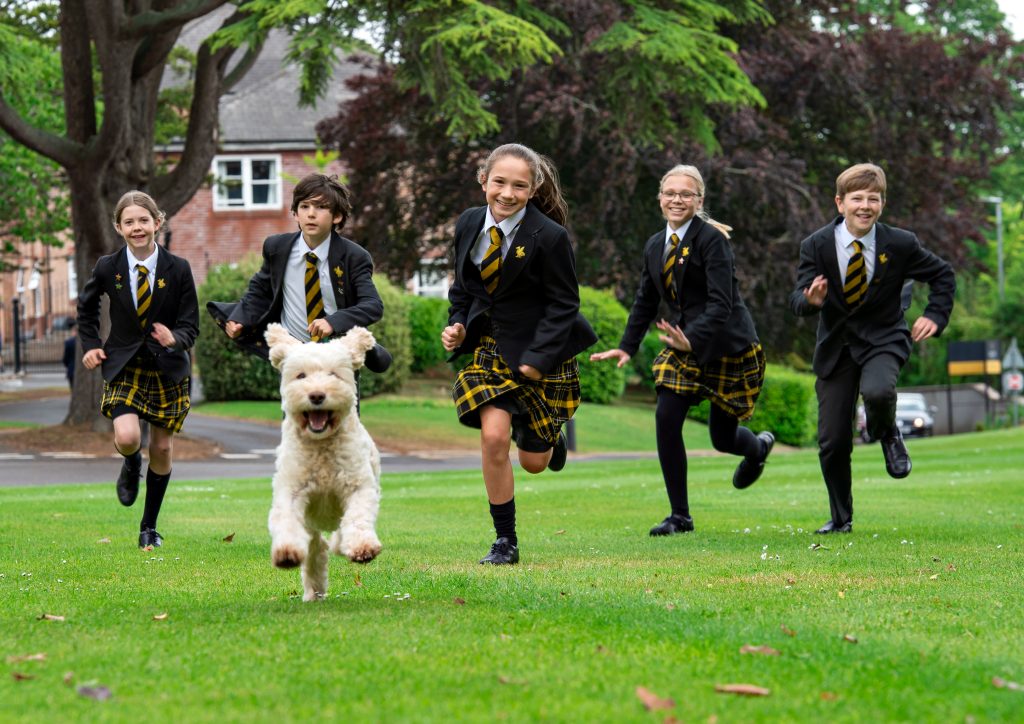 5 students running across the grass with a dog